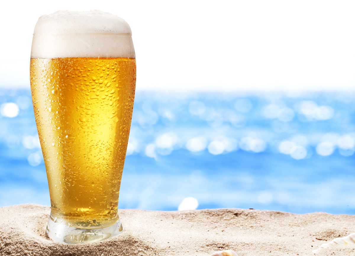 A glass of cold beer resting on the sand at a Caribbean beach