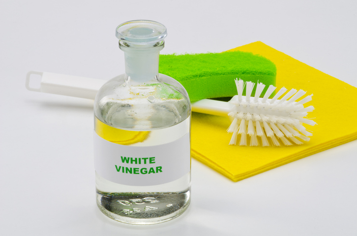Glass bottle of white vinegar in front of cleaning brushes.
