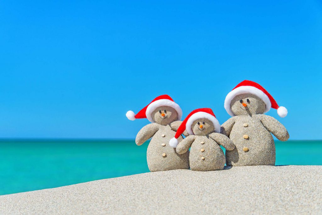 Family of Christmas Snowmen in santa hats at tropical beach.