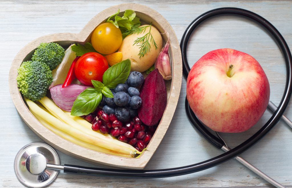 Findyello article on living a healthy lifestyle with bowl of fruits an apple and stethoscope.