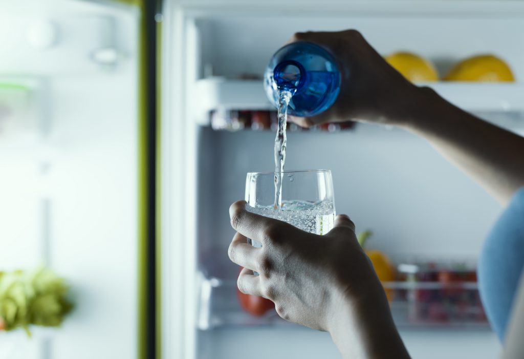 Woman taking a bottle of water from the fridge and pouring it into a glass
