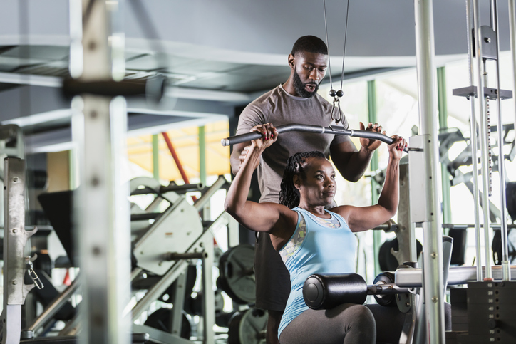Findyello article on gym tips for beginners with image showing a black woman working out with a trainer.