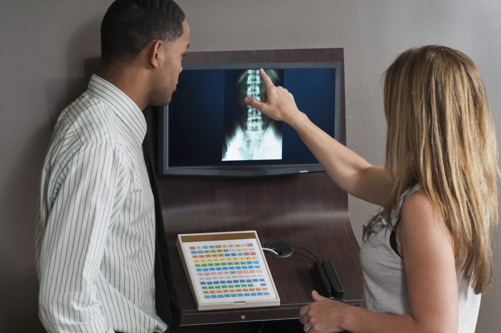 Findyello article on five types of holistic therapy with female chiropractor showing male patient a spine x-ray on the computer