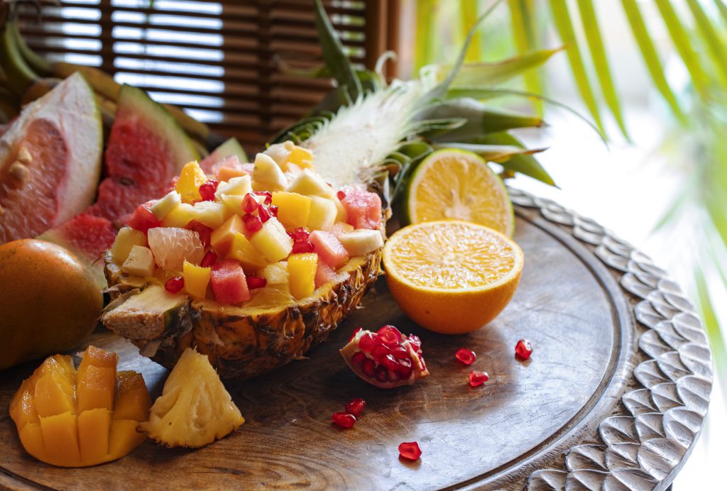Findyello article 12 months of fruit image shows fruit salad in half a pineapple on wooden table with sliced oranges, watermelon and mango