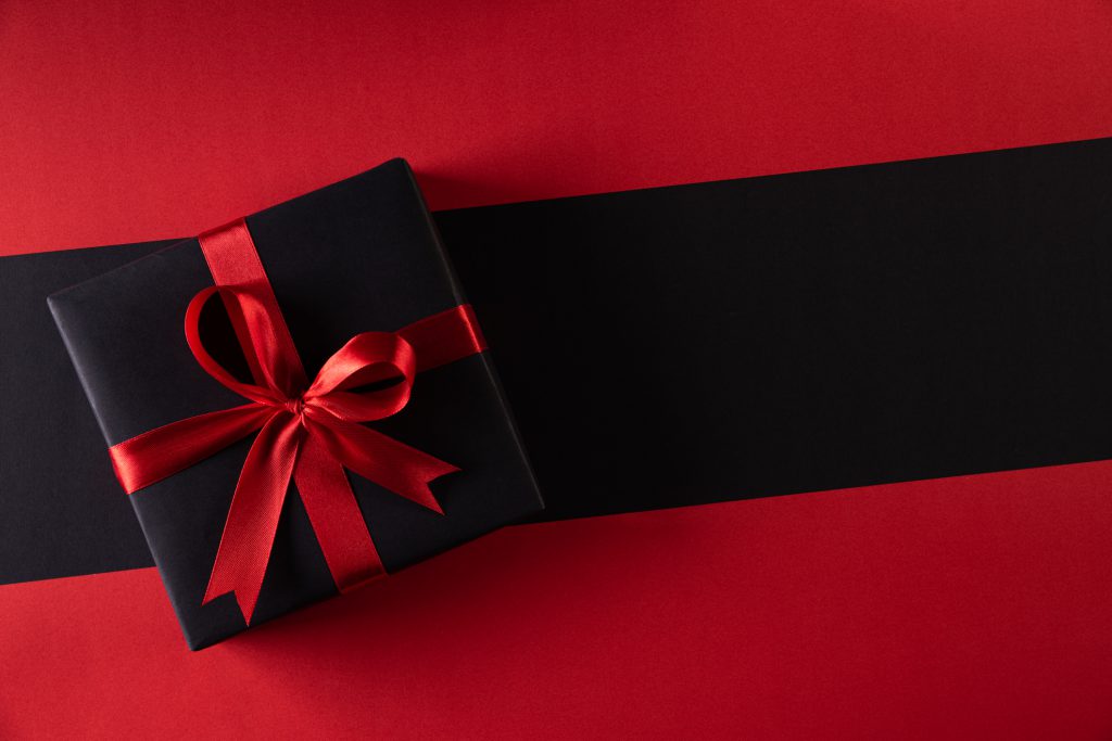 Black gift box with red ribbon on a black and red background. 