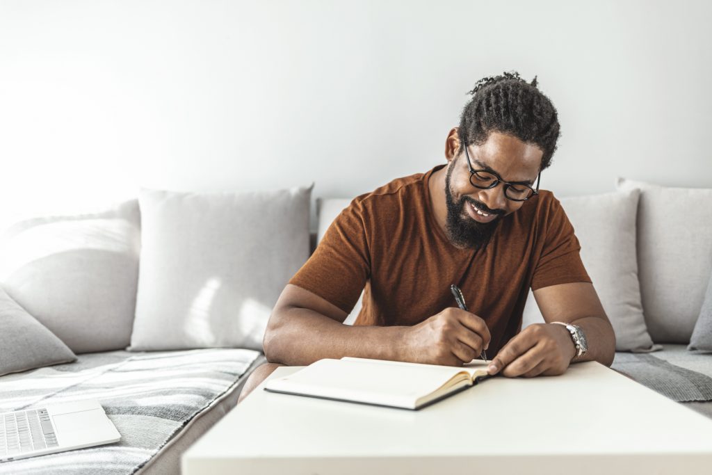 Findyello article on year in review image shows smiling African man with notepad and pen sitting on the sofa.