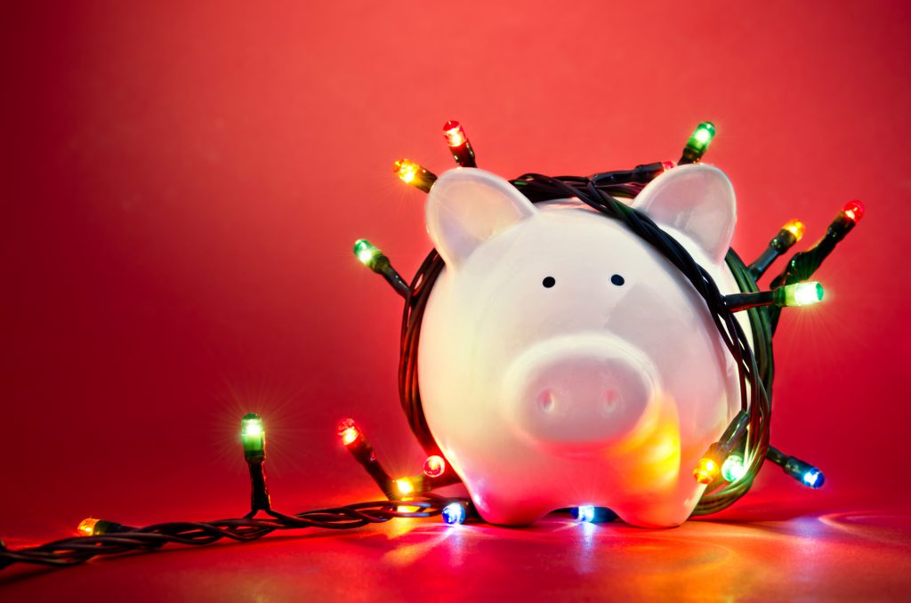 Pink piggy bank wrapped with Christmas lights on red background.