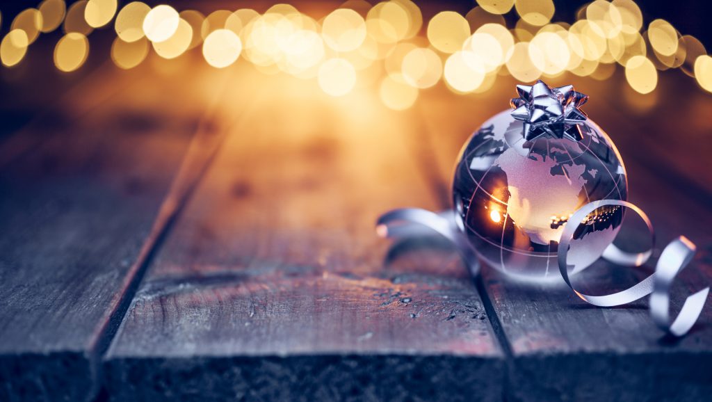 Earth glass globe and ribbon decorated on an old, wooden table. Defocused Christmas lights in the background