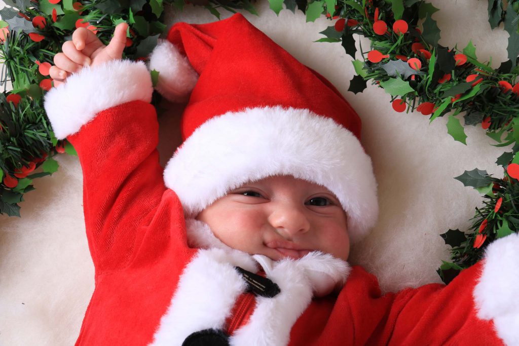 A grumpy newborn baby in a Santa Claus outfit