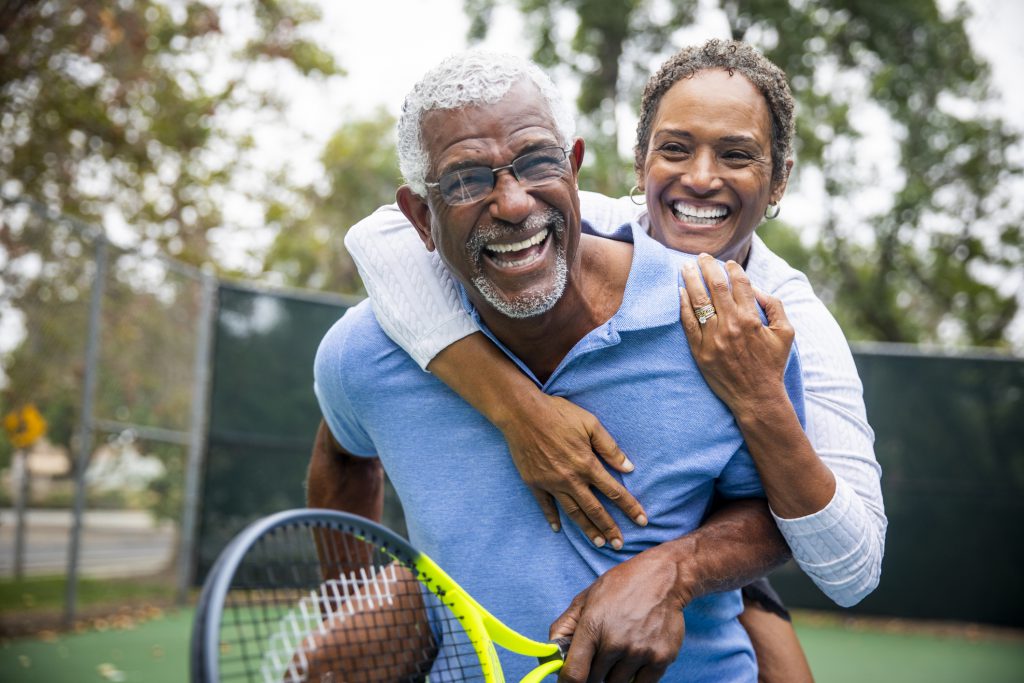 Findyello article on healthy lifestyles images shows a senior black couple piggyback together on the tennis court.