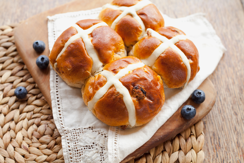 Findyello Easter article of hot cross buns recipe with image of four hot cross buns on a wooden platter with blueberries.